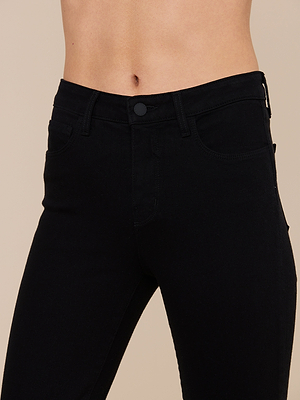 A close-up of a person wearing Kendra Cropped Flare Jeans in premium black denim, showing the waist and upper legs with a visible bare midriff against a plain beige background.