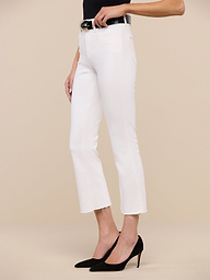 A person wearing the Kendra Cropped Flare Jean in white stretch denim with a raw hem, paired with a black top, a black belt featuring a gold buckle, and black pointed-toe heels stands against a plain white background.