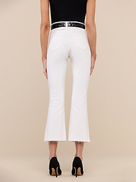 A person is standing facing away, wearing a black top, the Kendra Cropped Flare Jean in white stretch denim featuring a high-rise fit and raw hem, paired with black high-heeled shoes, against a plain white background.