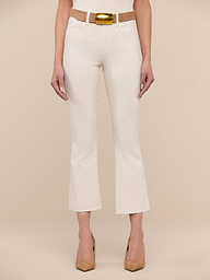 A woman stands facing forward, wearing the Kendra Cropped Flare Jean in vintage white, paired with a tan belt featuring a gold buckle and tan heels. The background is plain white.