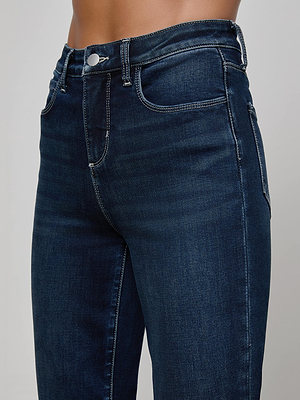 A close-up shows a person wearing L'AGENCE Kendra Cropped Flare Jean in dark wash super stretch denim, featuring white stitching, front pockets, belt loops, and a metal button closure. The focus is on the waist and upper legs.
