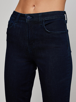A close-up shows a person wearing the L'AGENCE Kendra Cropped Flare Jean, featuring dark indigo wash, visible button, pockets, and belt loops, captured from waist to upper thighs.
