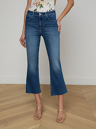 Wearing the Kendra Cropped Flare Jean in a dark denim wash, a person pairs it with a floral sleeveless top and beige heeled sandals while standing against a plain white background. Only the lower half of their body is visible.