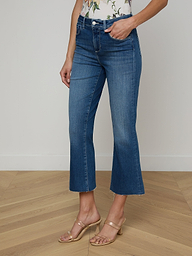 A person models the Kendra Cropped Flare Jean in a dark denim wash, paired with a floral top and beige heeled sandals, posing against a plain white background with only the lower half of the body visible.