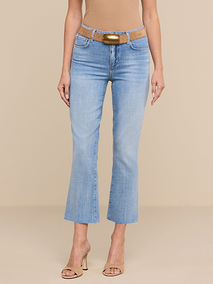 Wearing the Kendra Cropped Flare Jean in light wash denim with raw hems, a tan belt with a gold buckle, a sleeveless tan top, and beige heeled sandals, a person stands against a beige background.