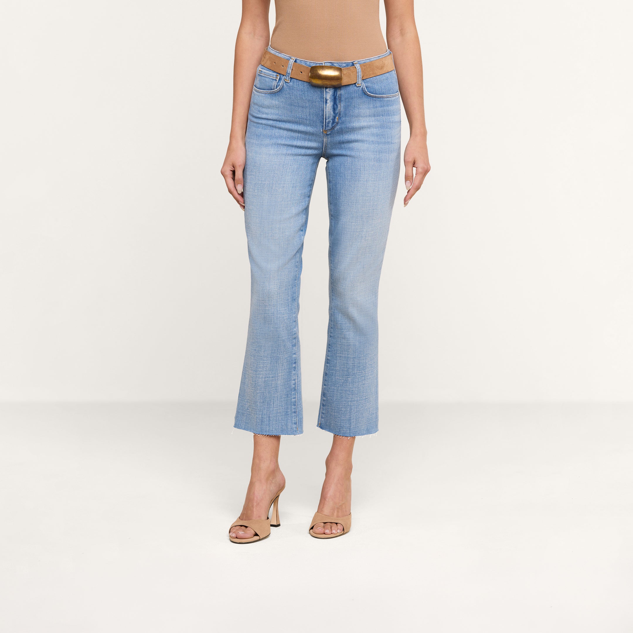 A person is shown from the shoulders down standing against a plain white background, wearing Kendra Cropped Flare Jean in a light wash, a tan sleeveless top, a matching tan belt, and tan high-heeled shoes. Their head is not visible.