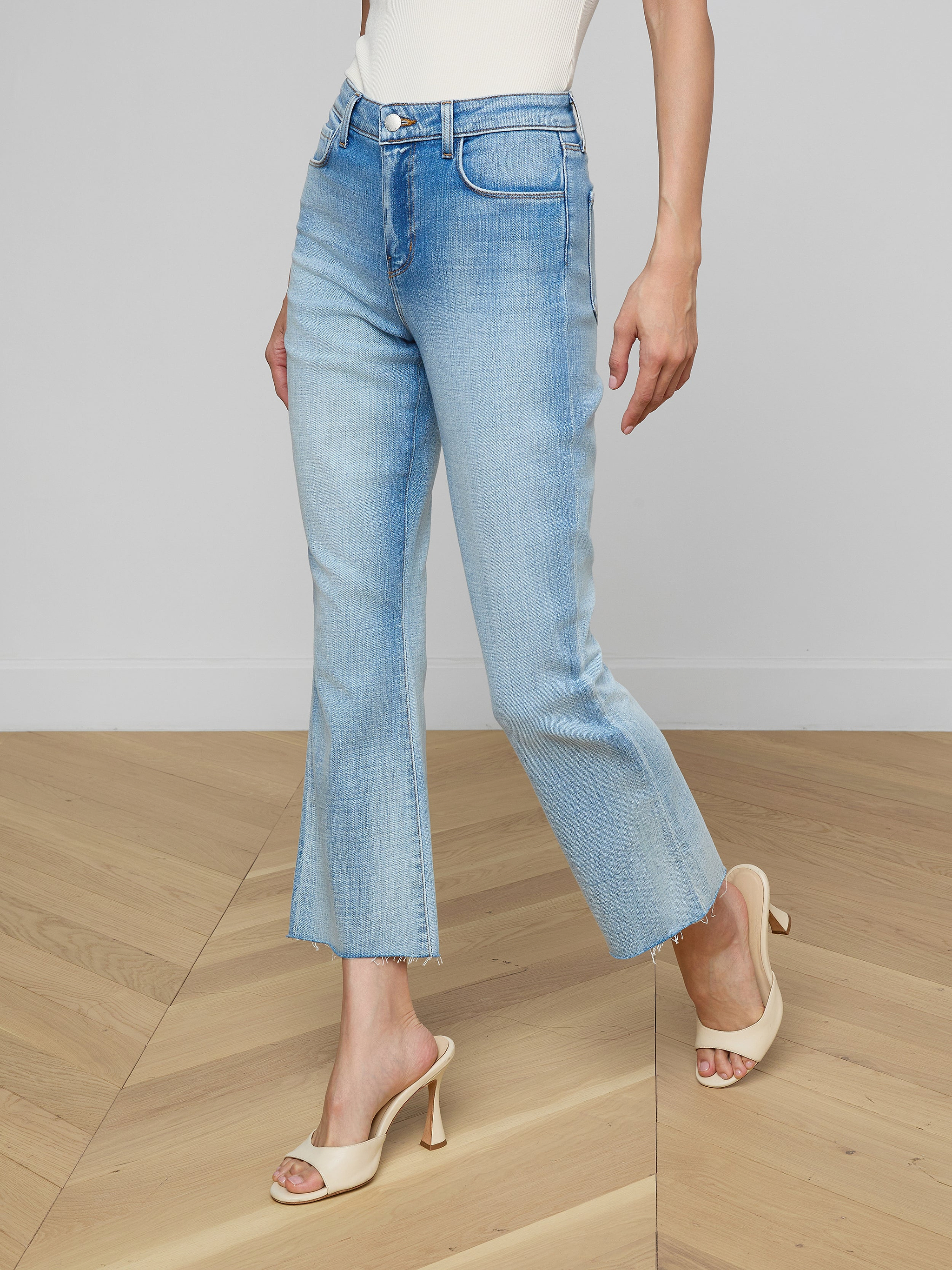 A person wearing the Kendra Cropped Flare Jean, a tan sleeveless top, a brown belt, and beige high-heeled sandals stands against a plain white background. Their head and lower arms are not visible.