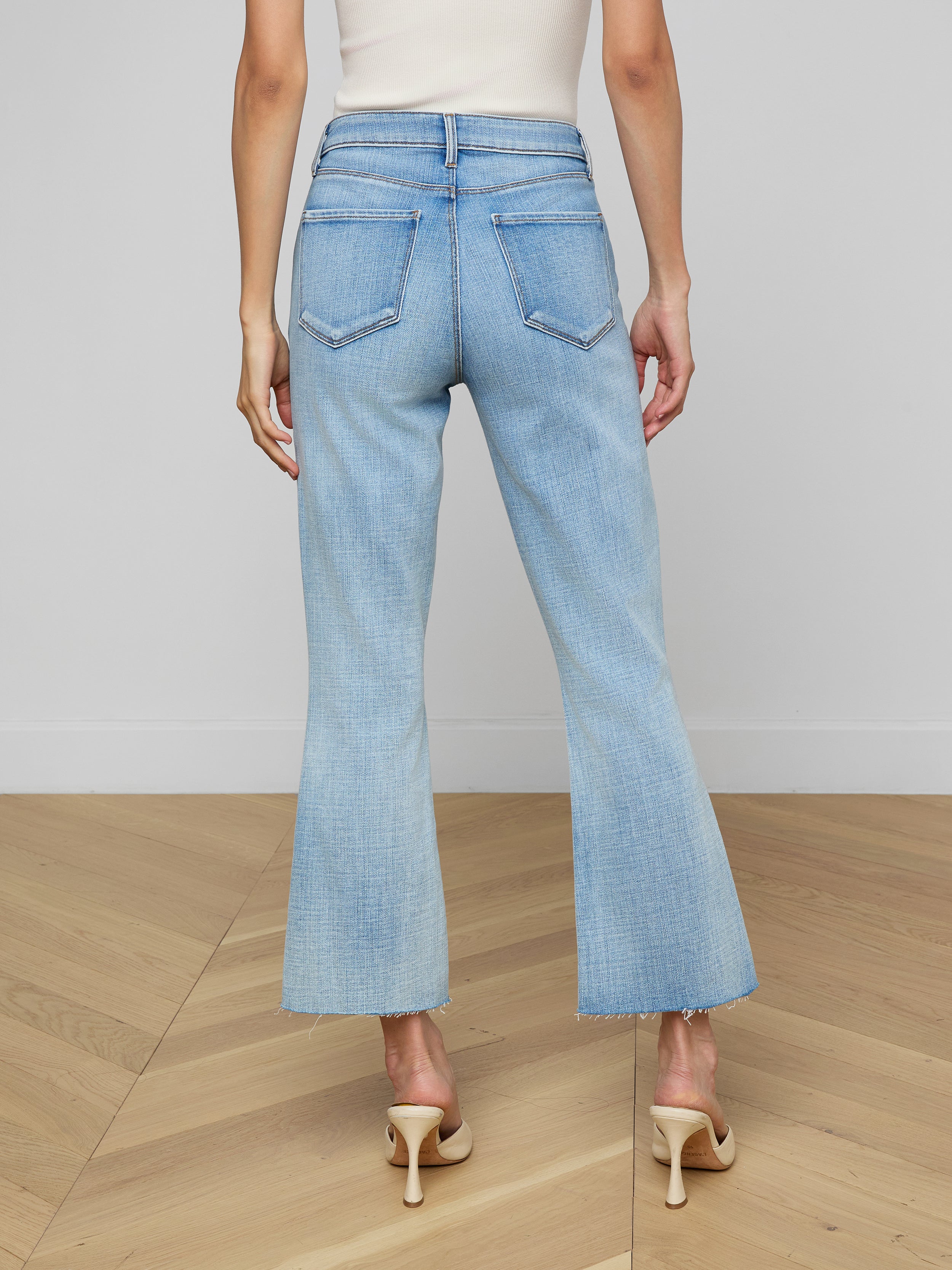 A person is shown from the back wearing the Kendra Cropped Flare Jean in a light wash, paired with a brown sleeveless top and beige heeled shoes, standing against a plain white background.