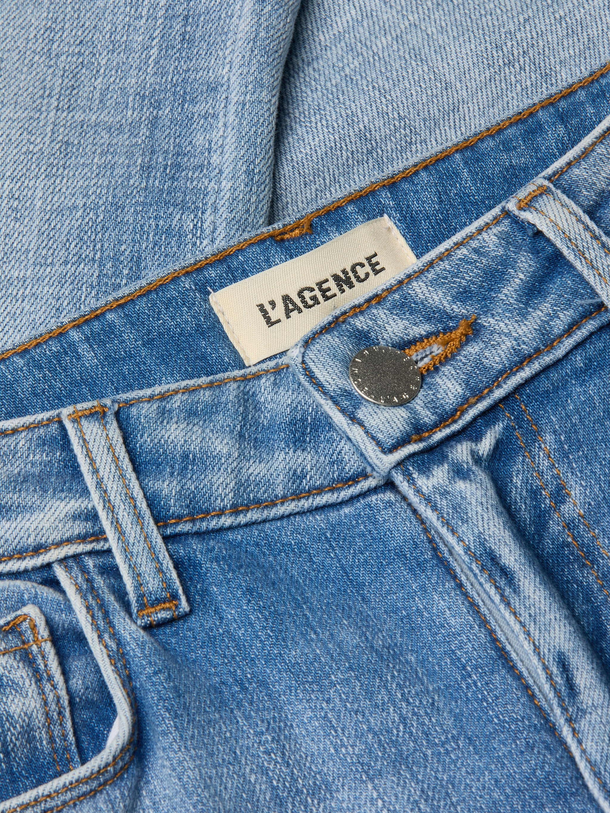 Close-up of light wash denim Kendra Cropped Flare Jean featuring an LAGENCE brand label near the waistband and a metallic button closure, highlighting its stylish cropped flare silhouette.