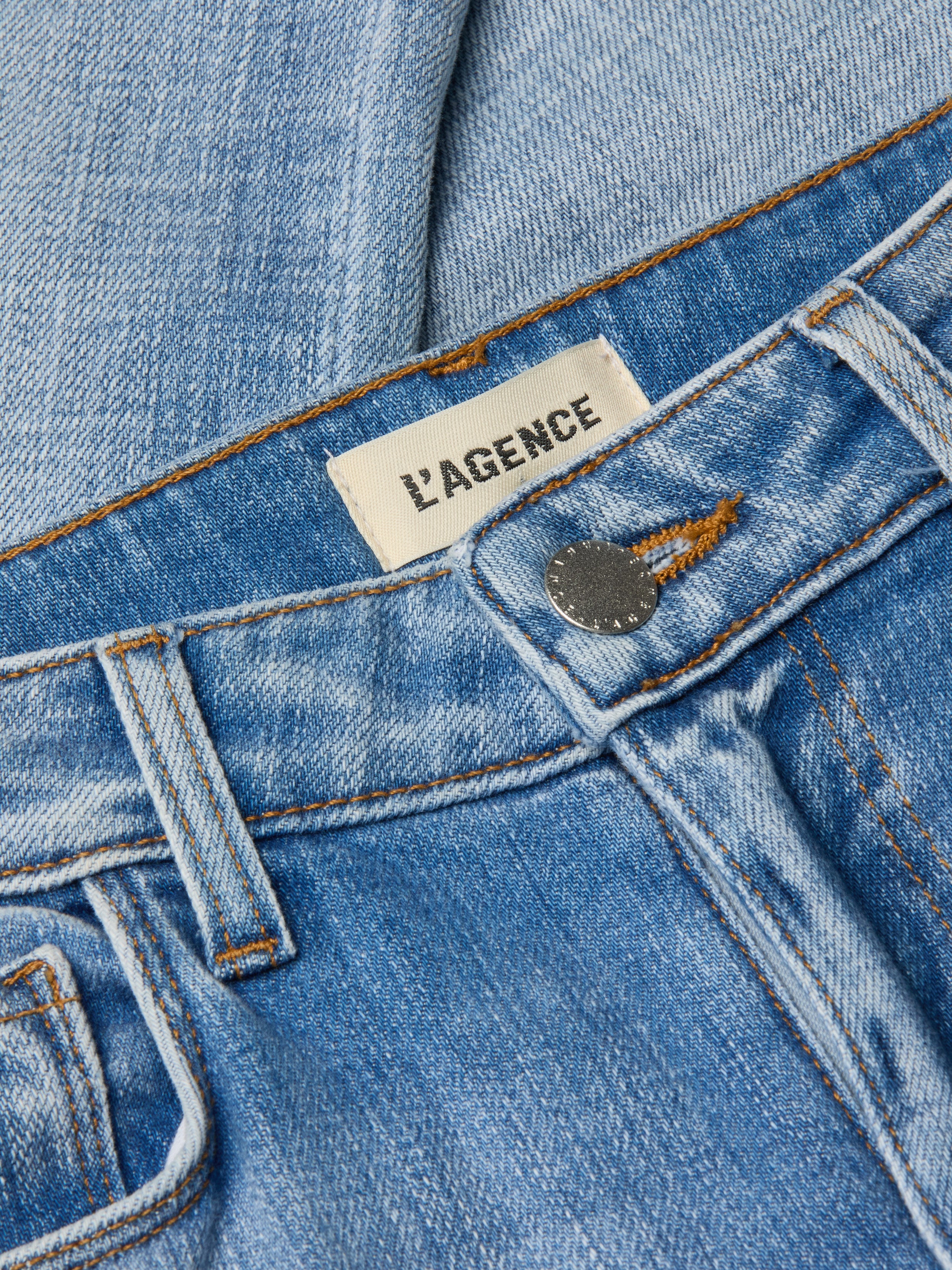 Close-up of light wash denim Kendra Cropped Flare Jean featuring an LAGENCE brand label near the waistband and a metallic button closure, highlighting its stylish cropped flare silhouette.