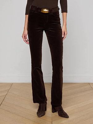 A person stands on a wooden floor in L'AGENCE Stevie Velvet Jean in coffee bean brown, styled with a matching top, belt, and brown heeled boots. The stretch velvet jeans feature a straight leg. Photo is cropped from the shoulders down.