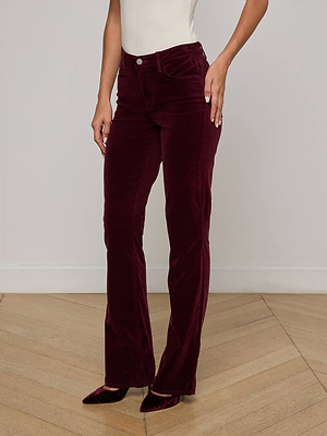 A person wears a white sleeveless top and L'AGENCE Stevie Velvet Jean—high-waisted, maroon stretch velvet pants with a straight leg fit—while standing on a wooden herringbone floor.