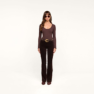 A woman wearing sunglasses, a long-sleeve dark java brown stretch velvet top, the Stevie Velvet Jean in brown with a belt, and brown shoes stands facing forward against a plain white background.
