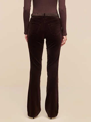 Model wearing the Stevie Velvet Jean in dark java brown—a high-waisted, slim straight leg stretch velvet pant—paired with a long-sleeve brown top, shown from the back against a plain beige background.