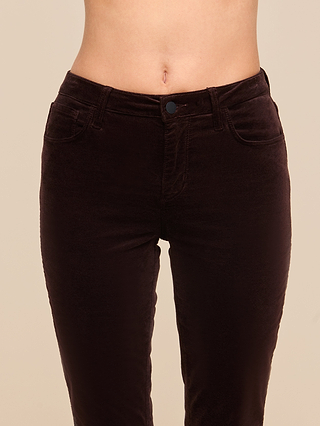 A person wearing the Stevie Velvet Jean in high-waisted, dark java brown stretch velvet with a slim straight leg, shown from the waist to mid-thigh and featuring a visible button and front pockets.