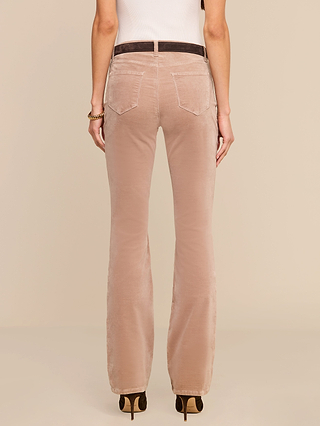 A person is seen from behind, standing against a plain beige background, wearing the Stevie Velvet Jean in light brown paired with a white sleeveless top.