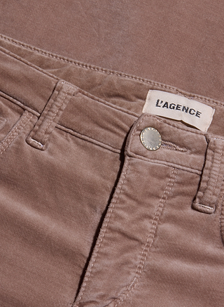 Close-up of Stevie Velvet Jean in tan, highlighting the waistband, belt loops, button, and a fabric label reading L’AGENCE. The high-rise stretch velvet fabric texture and stitching details are clearly visible.