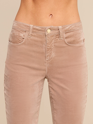 A close-up of a person wearing the Stevie Velvet Jean, a high rise stretch velvet pant in a light brown shade, focusing on the waist and upper thighs. These tan velvet jeans feature belt loops, front pockets, and a button closure.