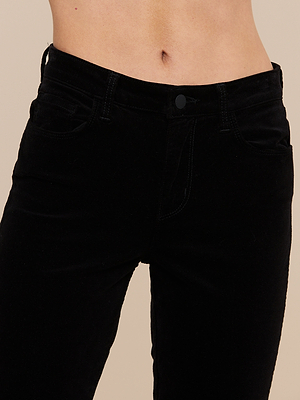 A close-up of a person’s lower torso wearing the Stevie Velvet Jean in black, highlighting the high-rise waistband, front pockets, and a visible navel against a neutral background.