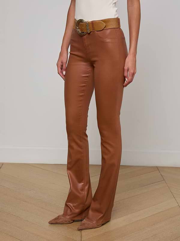 A person wearing the Selma Coated Bootcut Jean, styled with a tan belt and pointed-toe shoes, stands against a plain white background. Only the lower half of their body is visible.