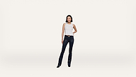 A woman stands confidently against a plain white background, wearing a sleeveless white top, black leather pants, and black shoes.