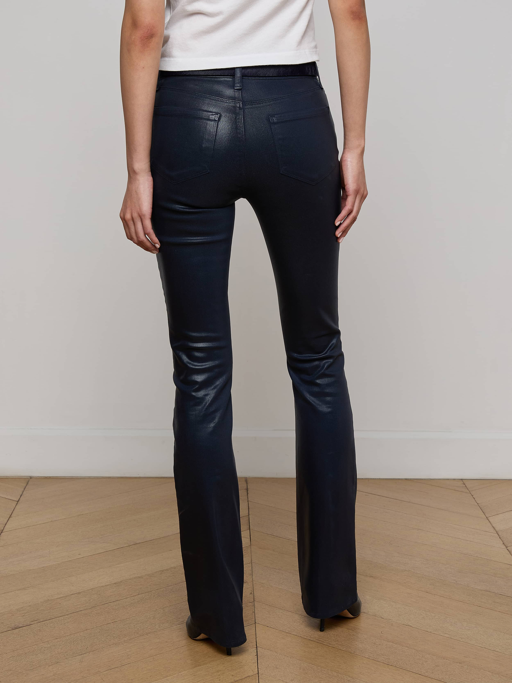 A person wearing the Selma Coated Bootcut Jean in black and a white top stands facing away, displaying the back view of the outfit against a plain white background.