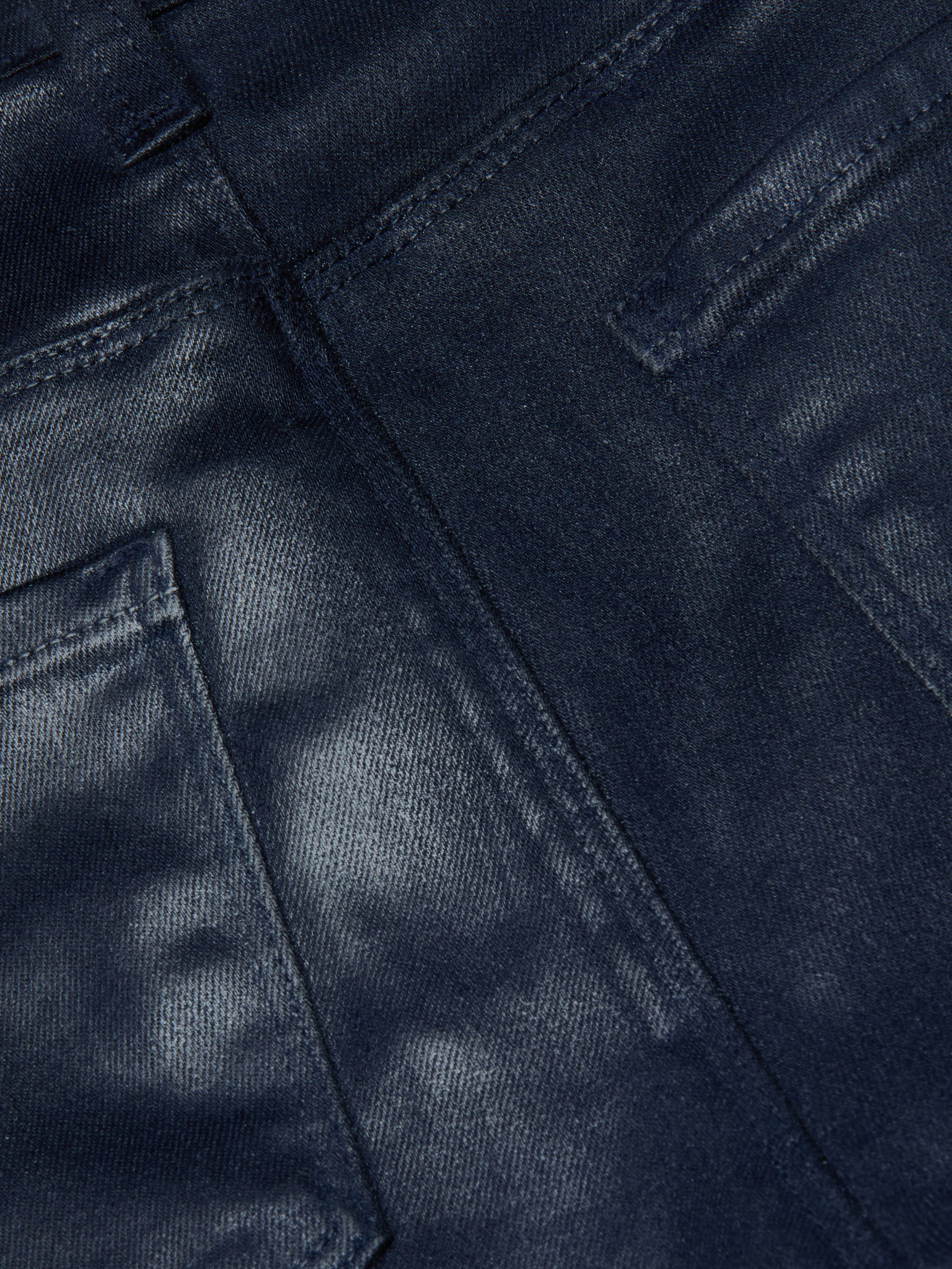 Close-up of the Selma Coated Bootcut Jean in dark blue, featuring detailed stitching and the edges of two back pockets, highlighting the texture and weave of its leather-alternative denim fabric.