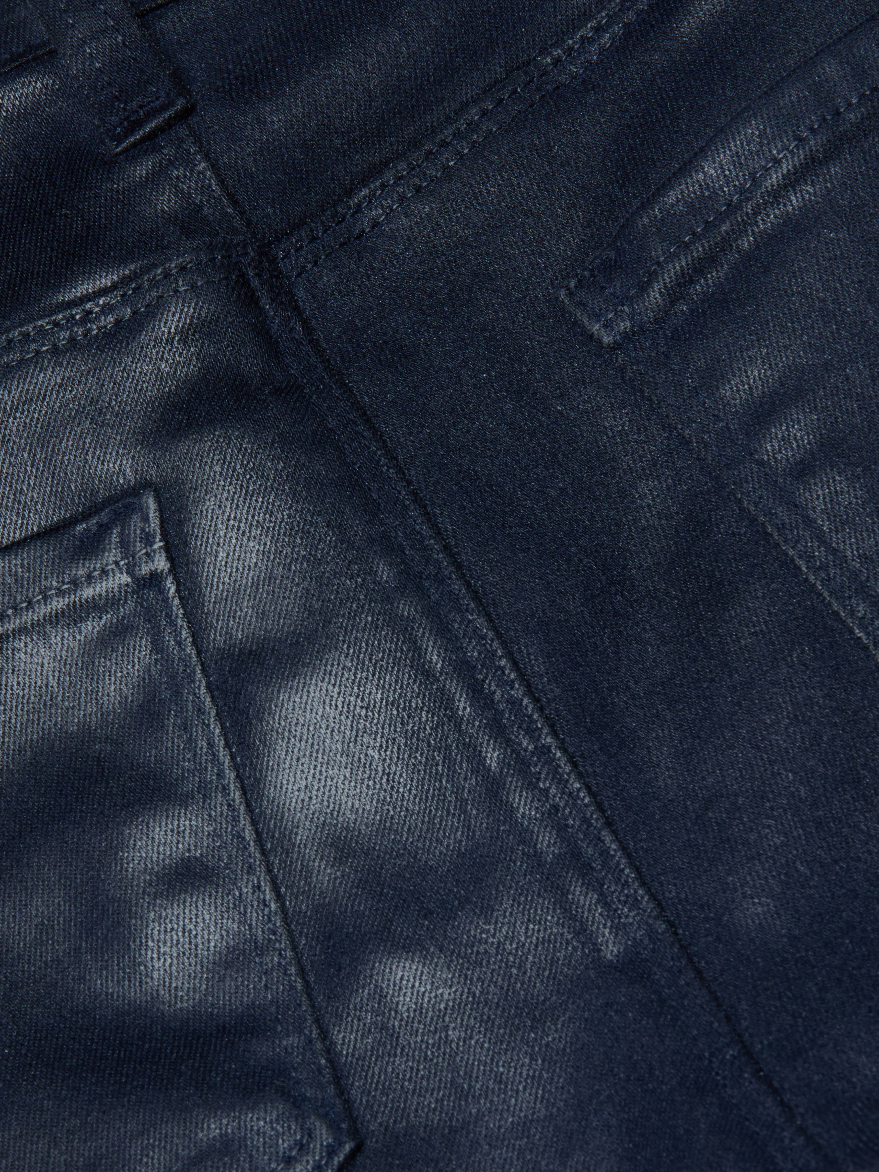 Close-up of the Selma Coated Bootcut Jean in dark blue, featuring detailed stitching and the edges of two back pockets, highlighting the texture and weave of its leather-alternative denim fabric.