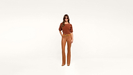 A woman wearing sunglasses, a rust-colored top, tan pants, and tan shoes stands stylishly against a plain white background.