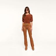 A woman wearing sunglasses, a dark java brown short-sleeve sweater, the Selma Coated Bootcut Jean with a belt, and brown shoes stands against a plain white background.
