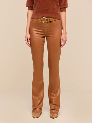 A person wearing the Selma Coated Bootcut Jean in dark java brown, paired with a matching brown sweater, a tan belt with a round buckle, and tan shoes, stands against a beige background.
