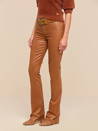 A person wearing the Selma Coated Bootcut Jean in dark java brown, paired with a brown textured sweater, a tan belt, and tan suede shoes, stands against a beige background. Only the body from shoulders down is visible.