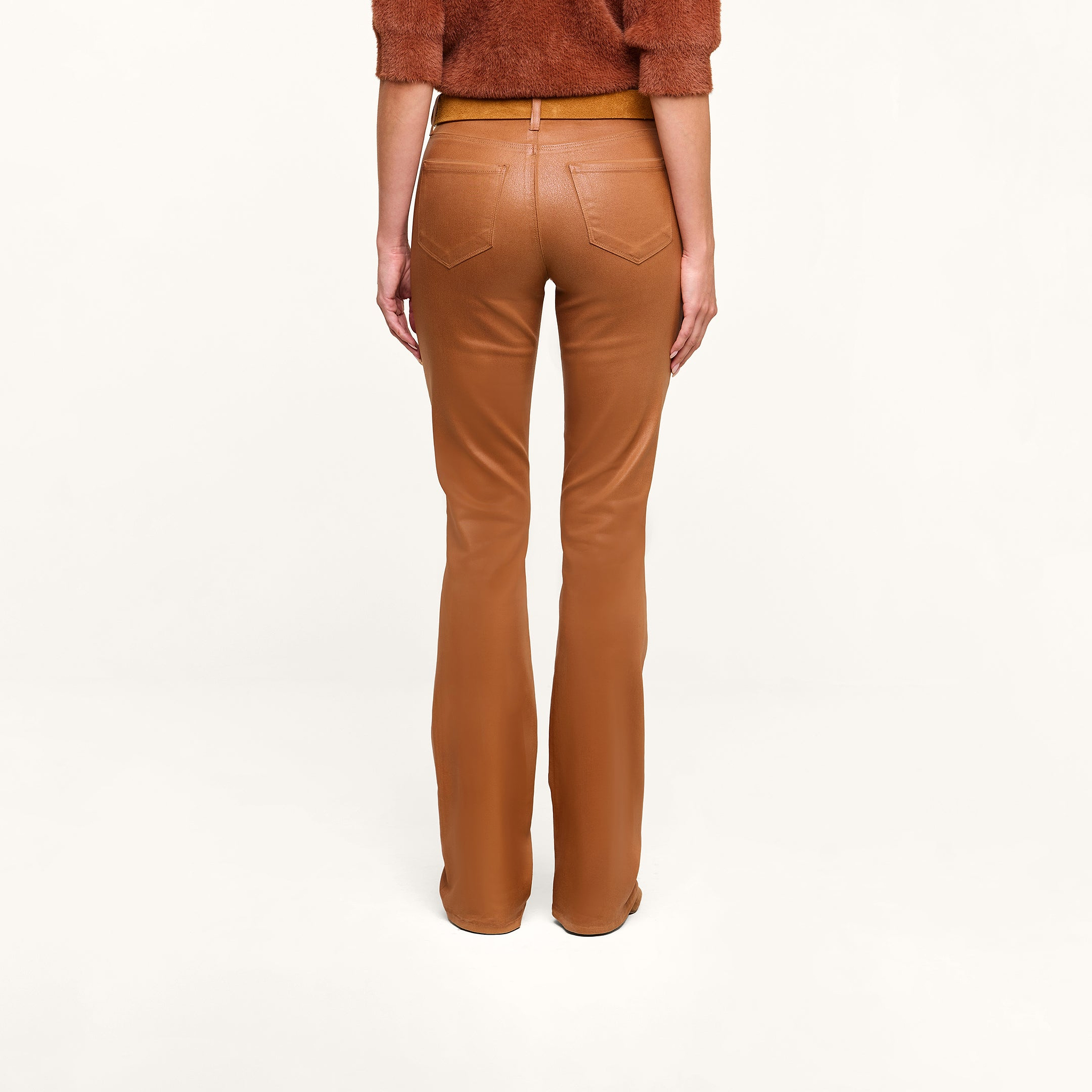 A person models the Selma Coated Bootcut Jean in a high-waisted, camel hue, paired with a dark java brown top, photographed from the back against a plain white background.