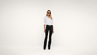 A woman wearing sunglasses, a white button-up shirt, and black pants stands against a plain white background.
