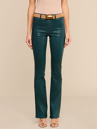 A person wearing the Selma Coated Bootcut Jean in teal with a super stretch fit, paired with a tan belt featuring a large buckle, a beige sleeveless top, and open-toed heels stands against a plain beige background.