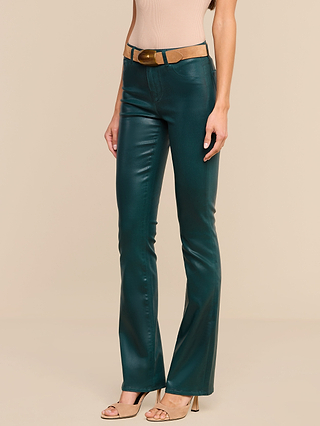 A person wearing the Selma Coated Bootcut Jean in teal, a beige sleeveless top, a tan belt with a large buckle, and beige open-toe heels stands against a plain beige background.