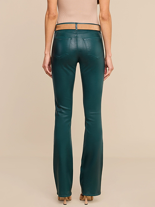A person stands facing away, wearing the Selma Coated Bootcut Jean in teal with a unique waistband and beige heeled sandals, against a plain beige background.