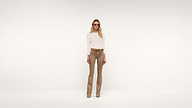 A person wearing sunglasses, a long-sleeve beige top, tan flared pants, and brown belt stands against a plain white background.