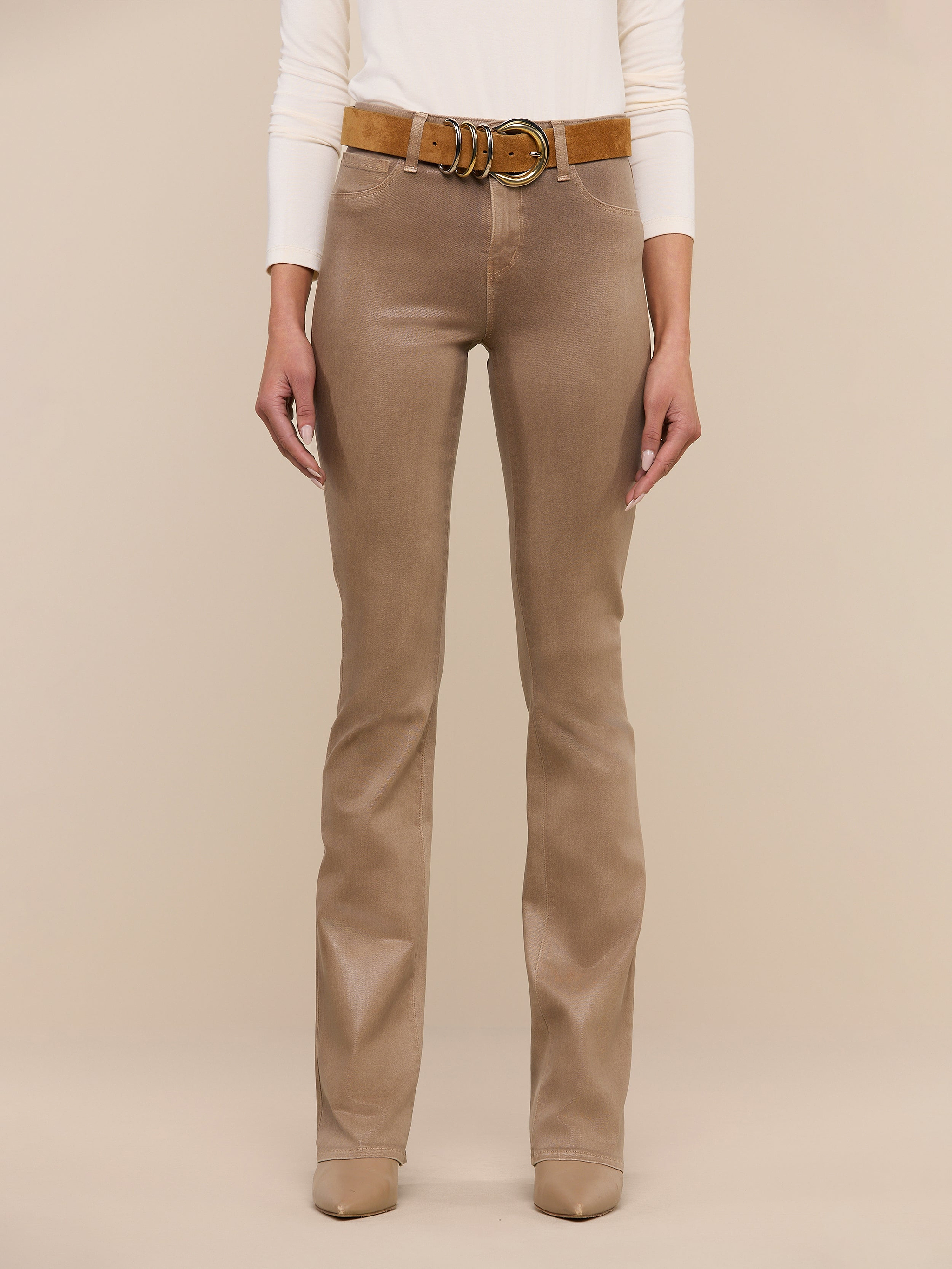 A person wearing the Selma Coated Bootcut Jean, styled with a brown belt and beige shoes, stands against a plain white background. Only the lower half of the body is visible.