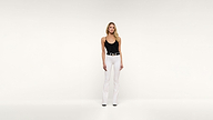 A woman wears a black camisole tucked into white flared trousers cinched with a black and gold belt.