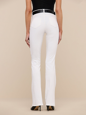 A person shown from the back against a beige background wears the Selma Bootcut Jean in white stretch denim, paired with a black textured belt and black high-heeled shoes.