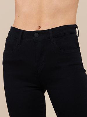 A close-up of a person wearing the Selma Bootcut Jean in black, showcasing the high-rise waist, hips, and upper thighs. The super stretch fit is highlighted with the jeans buttoned and the persons midriff visible.