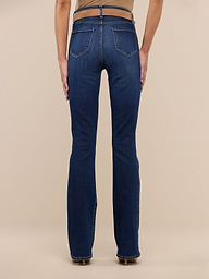 A person is standing facing away, wearing a beige sleeveless top, beige heels, and the Selma Bootcut Jean—a pair of dark blue high-rise slim bootcut jeans crafted from stretch denim—against a plain white background.