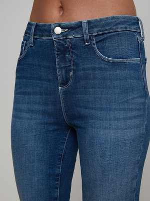 Close-up of a person’s midsection wearing the Selma Bootcut Jean—high-waisted blue denim with a contoured waistband, front pockets, and visible stitching—shown against a plain background.