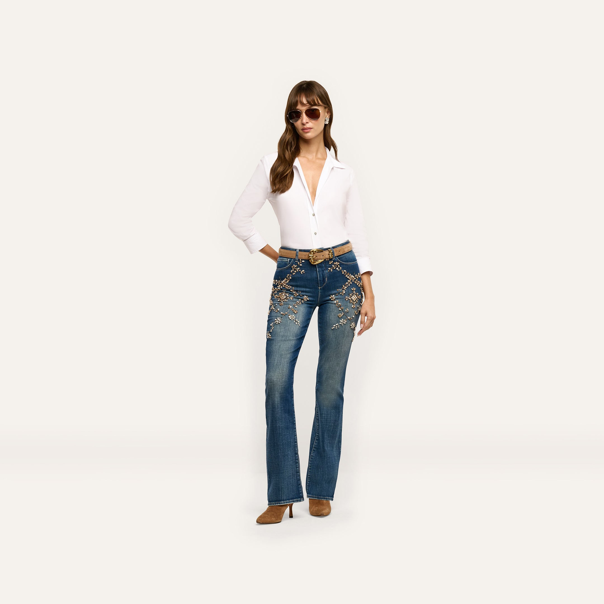 A model wearing a white button-down shirt and Selma Embellished Bootcut Jean with floral-shaped crystal details on the hips.