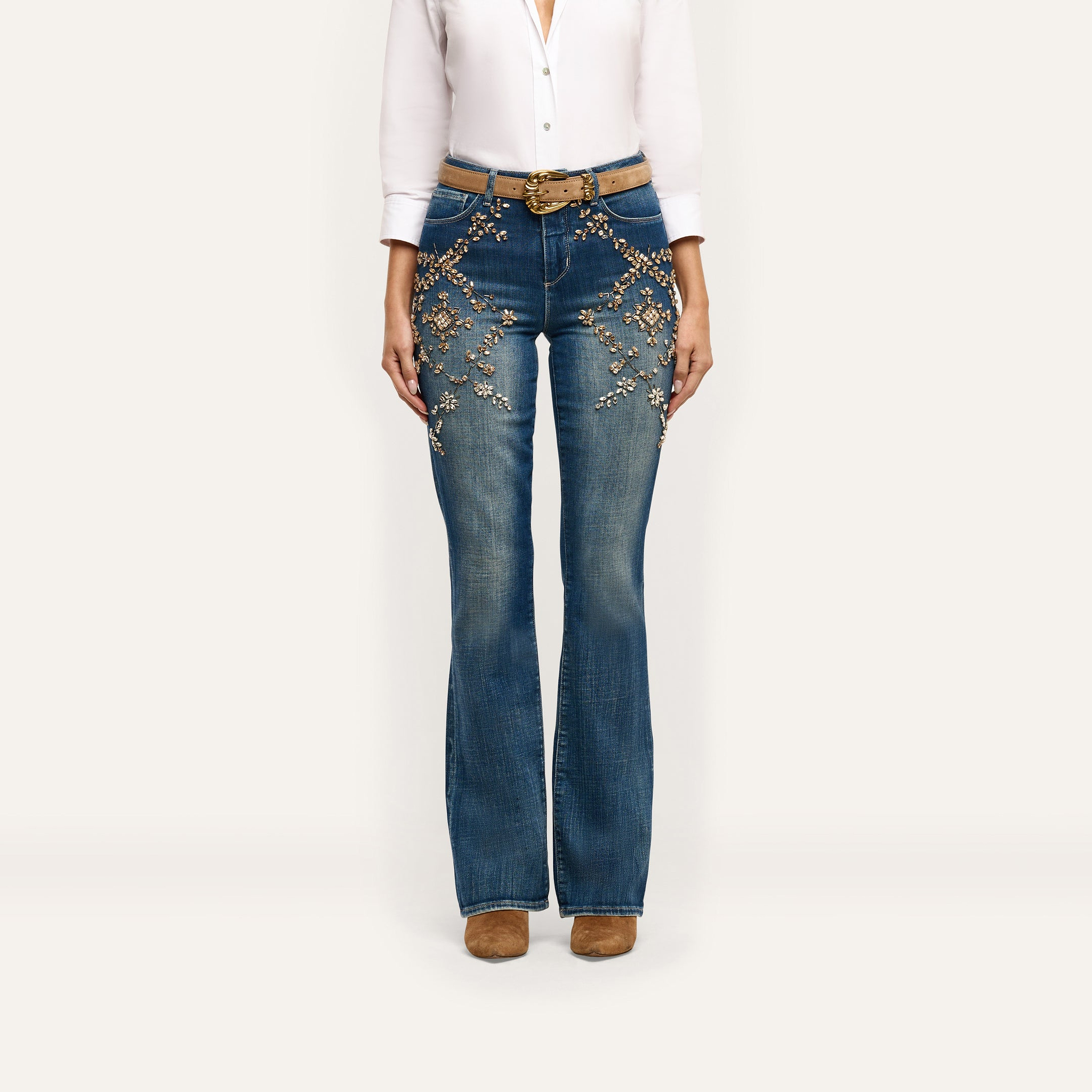Selma Embellished Bootcut Jean in blue, featuring floral embroidery and crystal details on the hips and thighs, worn with a tan belt and ankle boots.