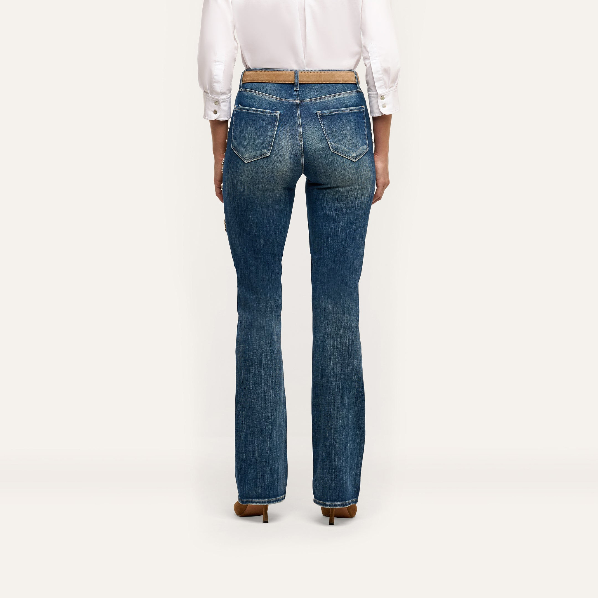 Rear view of blue Selma Embellished Bootcut Jean with crystal-embellished pockets, worn with a white button-down shirt and a thin tan belt.