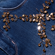 Close-up of blue denim Selma Embellished Bootcut Jean, featuring a floral pattern of amber-colored crystals and metal beads.