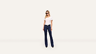 A woman in sunglasses, a plain white t-shirt, blue jeans, and black shoes stands facing forward against a light background.
