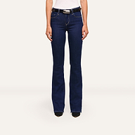 A person wears the Selma Bootcut Jean in dark blue stretch denim with a white top and black shoes, standing against a plain white background.